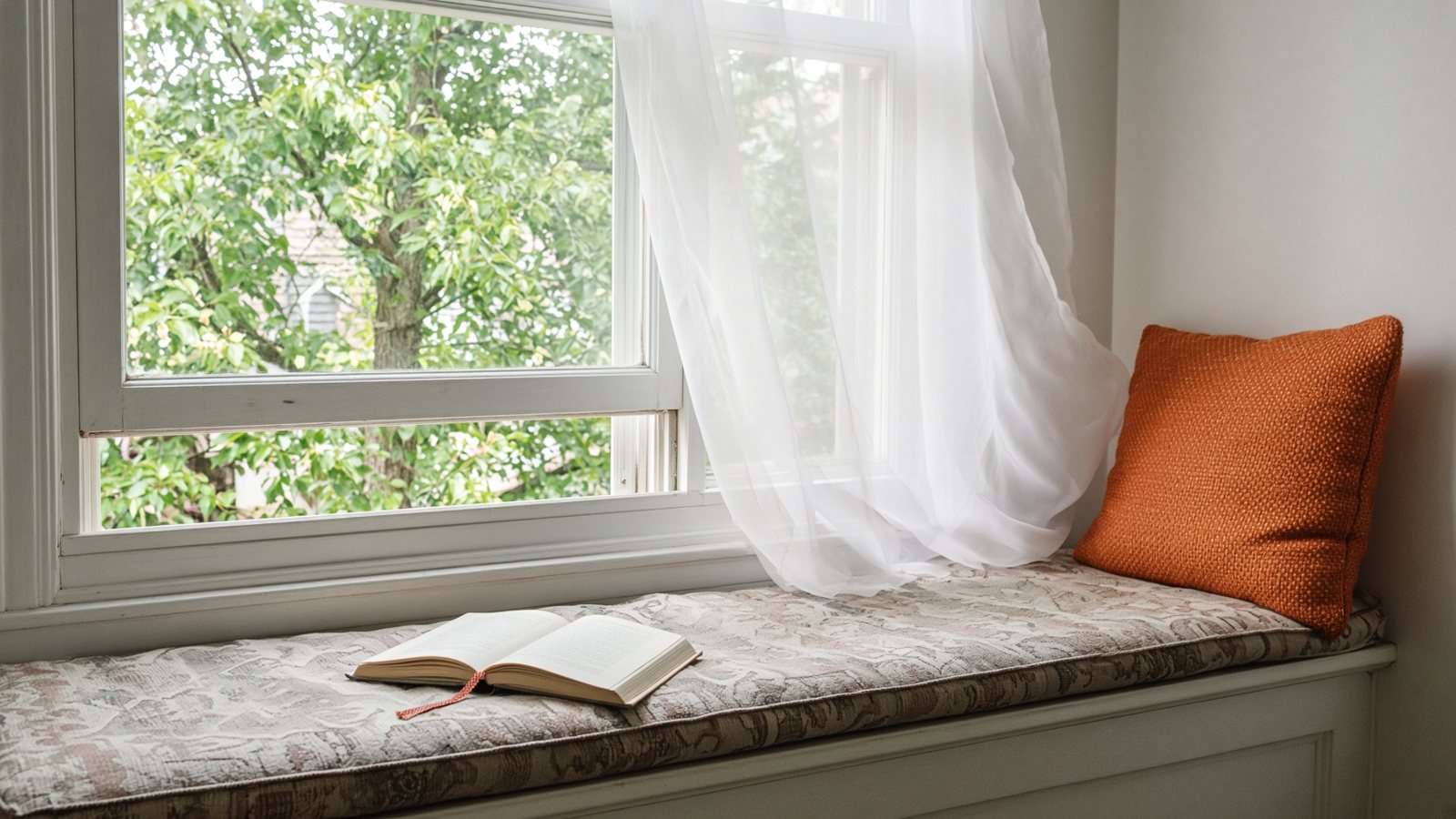 A living-room window seat, open window, a book left open